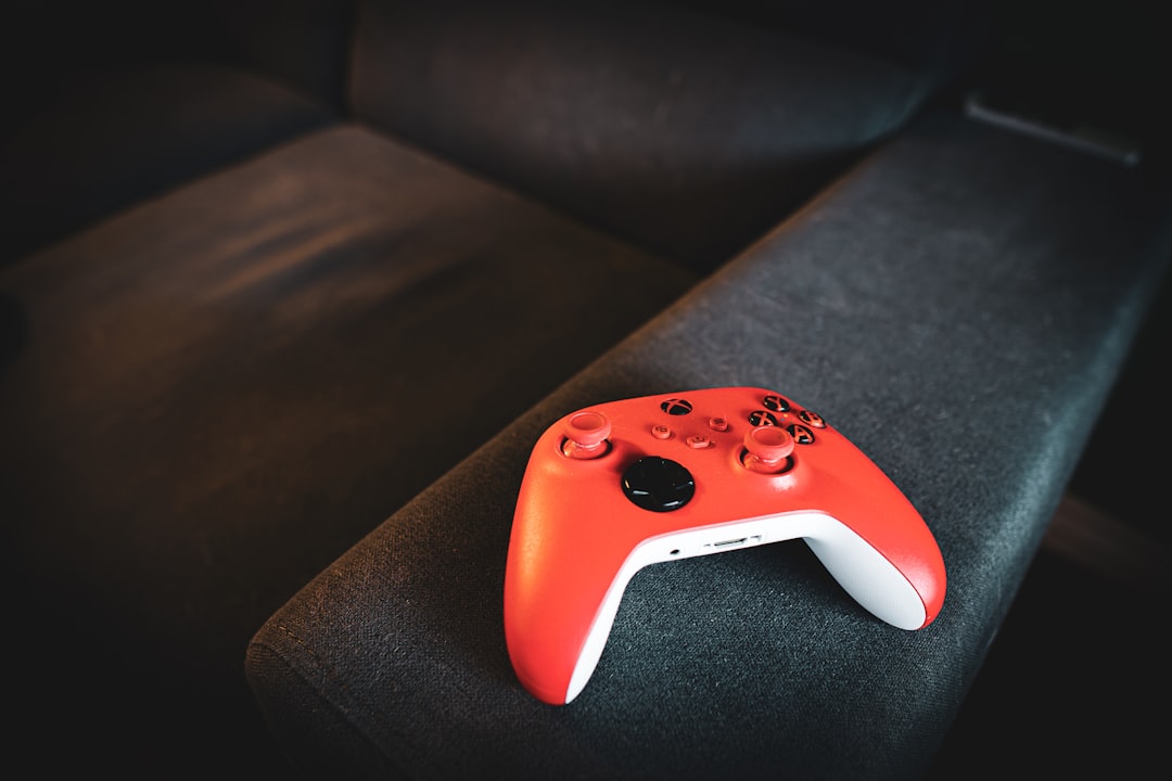 red-video-game-controller-rests-on-a-dark-couch-nrrgm9bgqyi